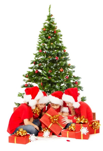 Weihnachtskinder in rotem weihnachtshut öffnung geschenkbox unter tanne über weißem hintergrund — Stockfoto