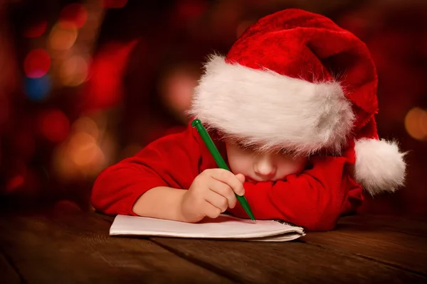 Christmas helper child writing letter in red Santa hat — Stock Photo, Image