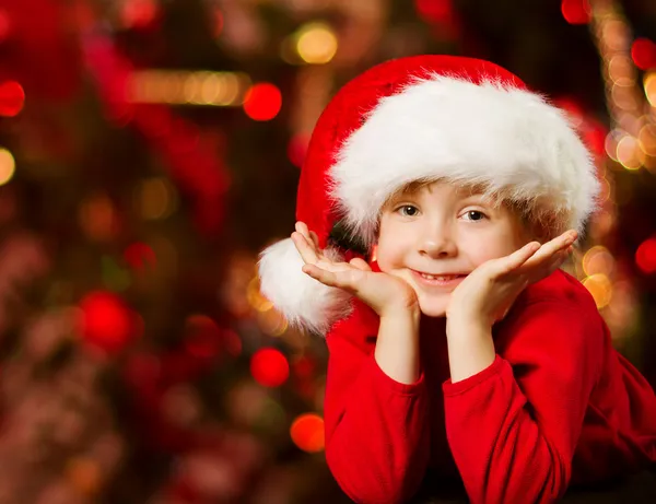 Christmas helper child in Santa hat smiling over red abstract backgroun — Stock Photo, Image