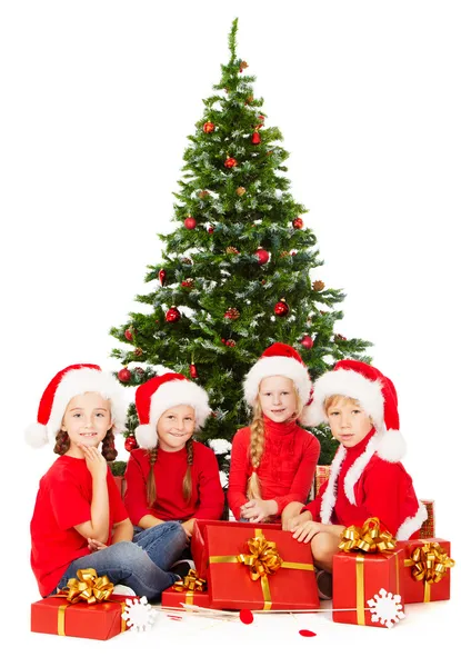 Kerstmis jonge geitjes in Kerstman hoed met presenteert vergadering onder fir tre — Stockfoto