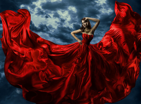 Woman in red evening dress, waving gown with flying long fabric over artistic sky background