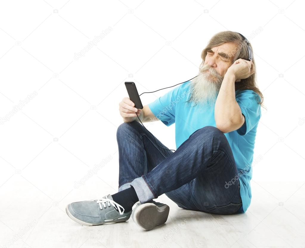 Senior man listening music in phone headphones. Old man with beard, edler sitting on floor isolated white background