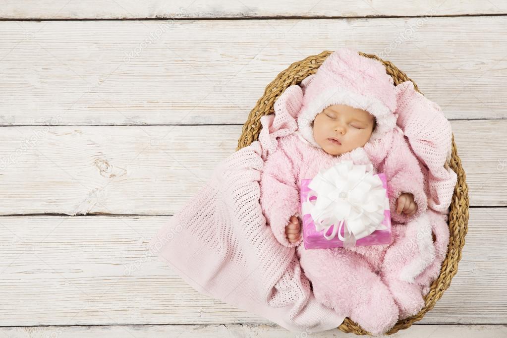 Baby girl with gift sleeping on wooden background, newborn in basket with present. Birthday party invitation card