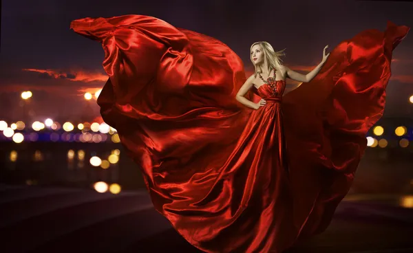 Femme dansant en robe de soie, robe de soufflage rouge artistique agitant et tissu scintillant, lampadaires nocturnes de ville Photos De Stock Libres De Droits