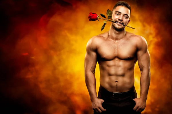 ティースでバラを持っているセクシーなボディビルダーの男 強いトップレス男性ホットフレイム芸術的背景に花を提示します バレンタインホリデーと愛のコンセプト — ストック写真