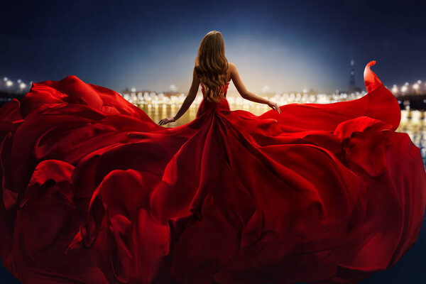 Fashion Woman in Red fluttering Dress Back Side Rear View. Glamour Model dancing with Long Silk Fabric flying on Wind over Night Sky City Light Landscape