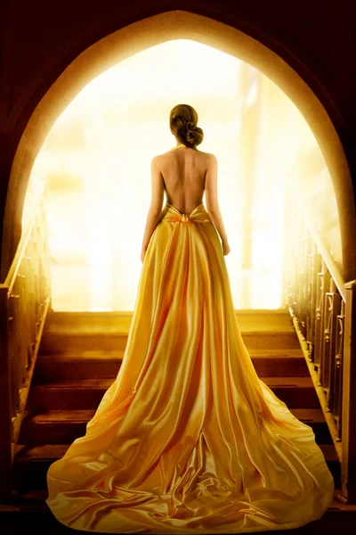 ゴールデンラグジュアリーガウンの女性シルエット バックサイドビュー裸で黄色の長いシルクのドレスでエレガントな女性 ファンタジーファッションモデルの女の子はドアウェイで光を見て — ストック写真