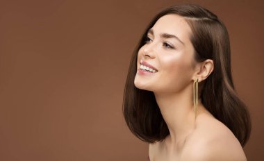 Gülümseyen Gülümseyen Model Yan Görünümü. Esmer, çıplak, makyajlı, kahverengi arkaplan üzerinde altın küpe olan bir kadın.