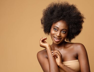 Afro saçlı Mutlu Afrika Güzellik Modeli. Koyu tenli ve bej üzerine siyah tüylü neşeli gülümseyen kadın. Face ve Vücut Bakımı
