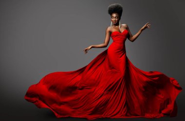 Kırmızı Uzun Sallanan Lüks Elbiseli Moda Modeli. Gri Arkaplan 'da dans eden Afro Siyah Saçlı Koyu Derili Güzel Kadın. Uçan kumaşlı İpek Gece Elbisesiyle Mutlu Afrikalı Seksi Kız