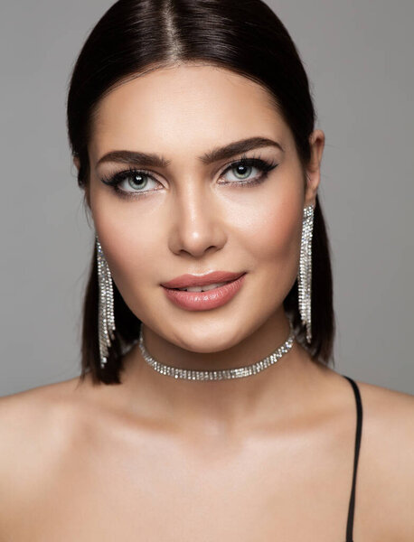 Fashion Beauty Woman Portrait with Silver Jewelry Earrings and Necklace. Glamour Model with Perfect Make up and Smooth Face Skin over Gray Background. Women Portrait with Diamond Jewellery Accessories