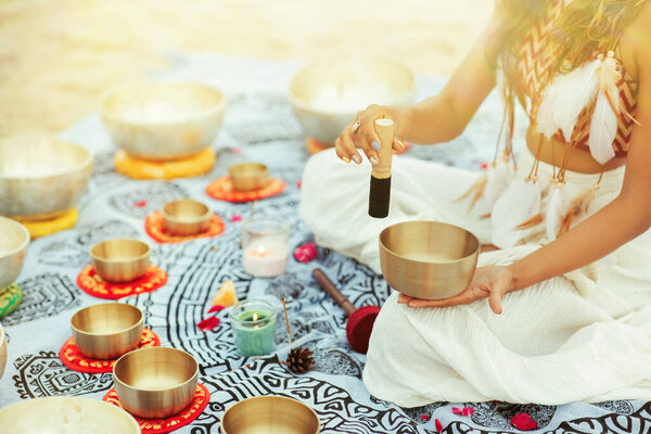 Женщина, играющая в Тибетские Поющие Чаши с Маллетом на пляже. Расслабляющий музыкальный медитативный массаж и массаж звукового исцеления. Духовная практика йоги на солнечном фоне