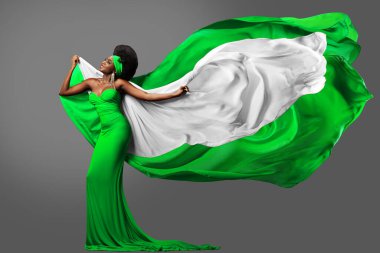 Yeşil Beyaz Elbiseli Kadın, Nijerya Bayrağı 'yla dans ediyor. Uzun elbiseli Afro saçlı, uçan ipek eşarplı Moda Modeli. Gri üzerinde şifon kumaş sallıyor. Nijerya Bağımsızlık Günü