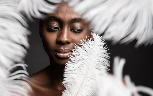 Black Woman Face with White Feather. Afro Beauty Model Face Skin Care and Cosmetics. Dark Skinned Women Fashion Portrait over Gray background