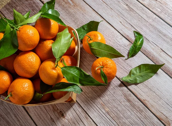 Tahta bir yüzeyde yeni toplanmış mandalinalarla dolu sepet.