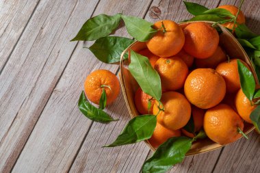 Tahta bir yüzeyde yeni toplanmış mandalinalarla dolu sepet.