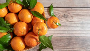 Tahta bir yüzeyde yeni toplanmış mandalinalarla dolu sepet.