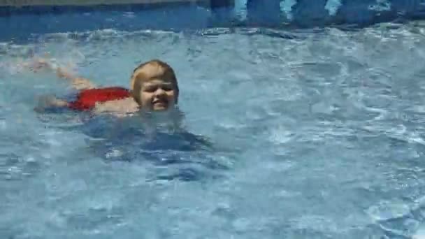 Маленький хлопчик плаває в басейні в спекотний сонячний день — стокове відео