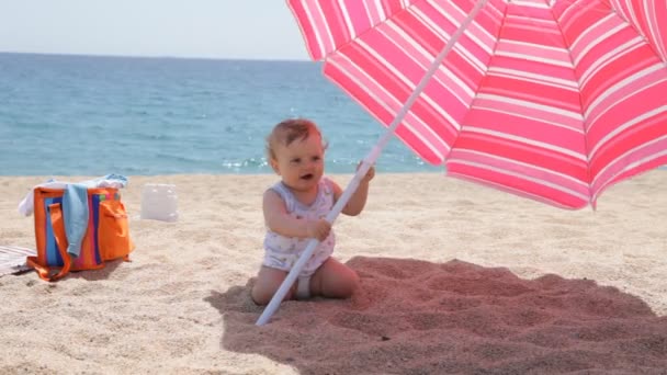 Lächelndes Baby mit Sonnenschirm am Strand — Stockvideo