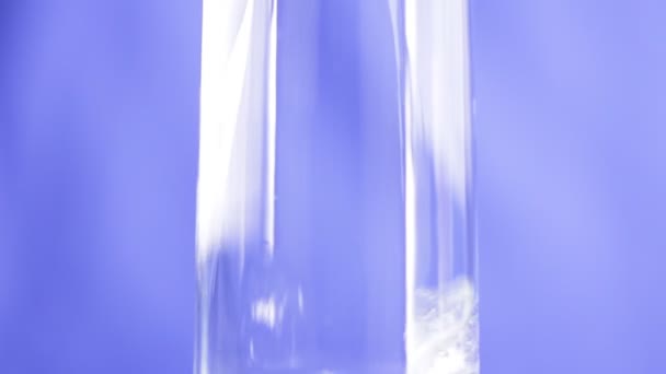 Νερό ρίχνει σε ποτήρι σε μπλε φόντο — Αρχείο Βίντεο