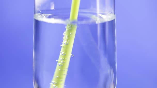 Acqua potabile dal bicchiere con una cannuccia verde su fondo blu — Video Stock