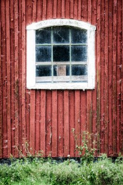 A very aged and weathered old red barn window facade at Ekeby in Sweden.