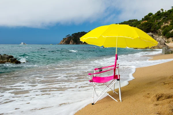Guarda-sol amarelo e cadeira rosa na praia — Fotografia de Stock