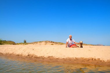 Yaşlı adam yaşlı köpekle yaz kumsalında yatıyor.