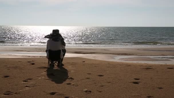 Senior homem sentado na praia assistindo por do sol — Vídeo de Stock