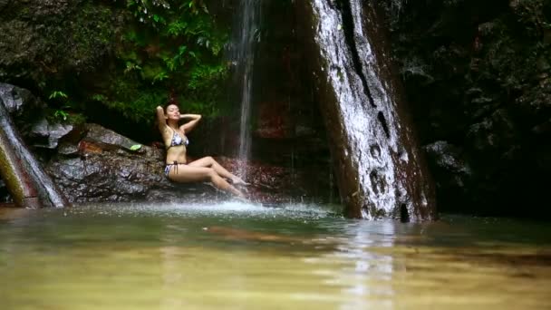 Сексуальная девушка в бикини, лежащая в водопаде — стоковое видео