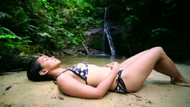 Σέξι κορίτσι με μπικίνι ξαπλωμένοs κάτω στον ποταμό καταρράκτη — Αρχείο Βίντεο