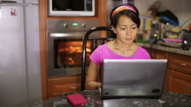 Mujer sentada con portátil por horno en la cocina — Vídeos de Stock