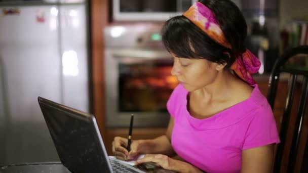 Mujer con portátil receta de escritura de Internet en la cocina — Vídeos de Stock