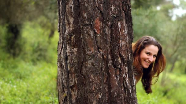 Bella ragazza guardando la fotocamera dietro l'albero — Video Stock