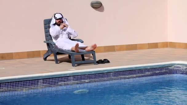 Saudi arabian man talking on phone at swimming pool — Stock Video