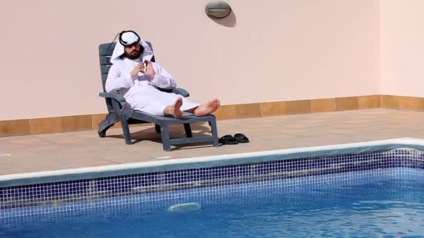 Hombre árabe saudí usando su teléfono en la piscina — Vídeos de Stock
