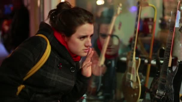 Mujer joven mirando a la ventana de la tienda de guitarra — Vídeo de stock