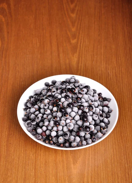 Heap of frozen black currant in a plate on the wooden surface — Stock Photo, Image