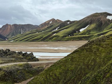 Laugavegur 'daki Landmannalaugar dağları dramatik gökyüzü, renkli yanardağ, lav tarlaları ve İzlanda' daki bir grup yürüyüşçü ile yürüyüş parkurunda.