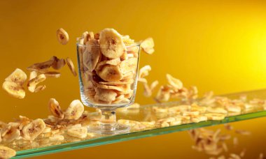 Muz cipsleri cam kaseye düşer. Kopyalama alanı olan sarı arkaplan.