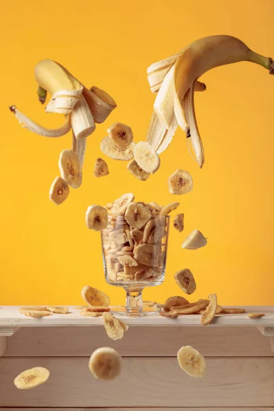 Chipsy Bananowe Wpadają Szklanego Kubka Żółtym Tle — Zdjęcie stockowe