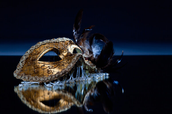  маска с пером на зеркальном столе
