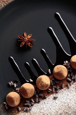 Çikolatalı trüf mantarı, siyah tabakta, çikolata soslu. Tatlılar kakao tozu ve pudra şekerle serpiştirilir. Üst görünüm. 