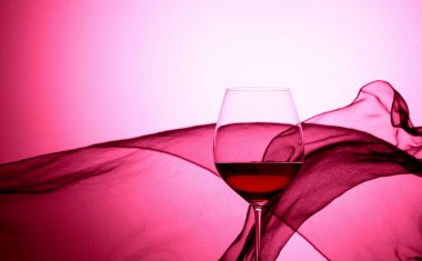 Sallanan saten perdenin arkasında bir kadeh kırmızı şarap. Mor arka plan.