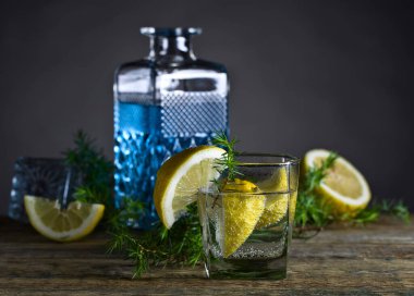 Eski ahşap bir masada mavi cin, tonik ve limonlu kokteyl. Limon dilimleri ve ardıç dalıklı alkol içeceği. Boşluğu kopyala.