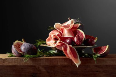 İncirli jambon, biberiye ve eski ahşap bir masada kırmızı zeytin. Boşluğu kopyala.