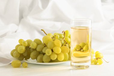 Beyaz bir masada bir bardak üzüm suyu ve üzüm suyu..