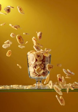 Muz cipsleri cam kaseye düşer. Kopyalama alanı olan sarı arkaplan.