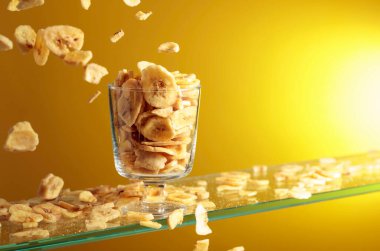 Muz cipsleri cam kaseye düşer. Kopyalama alanı olan sarı arkaplan.