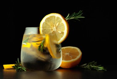 Limon dilimleri ve siyah arka planda biberiyeli kokteyl cin toniği. Boşluğu kopyala.